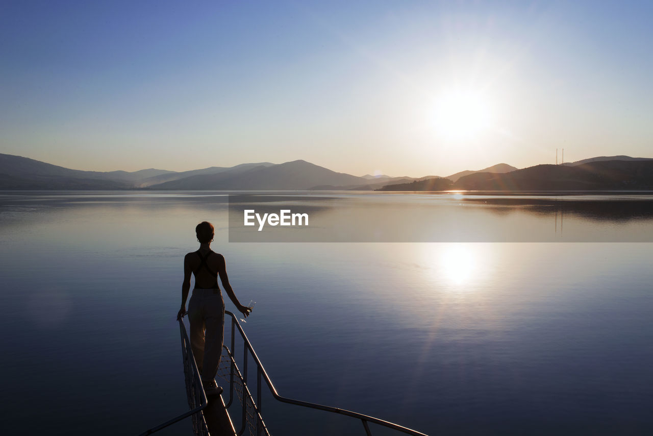 SILHOUETTE MAN ON LAKE AGAINST SKY AT SUNSET