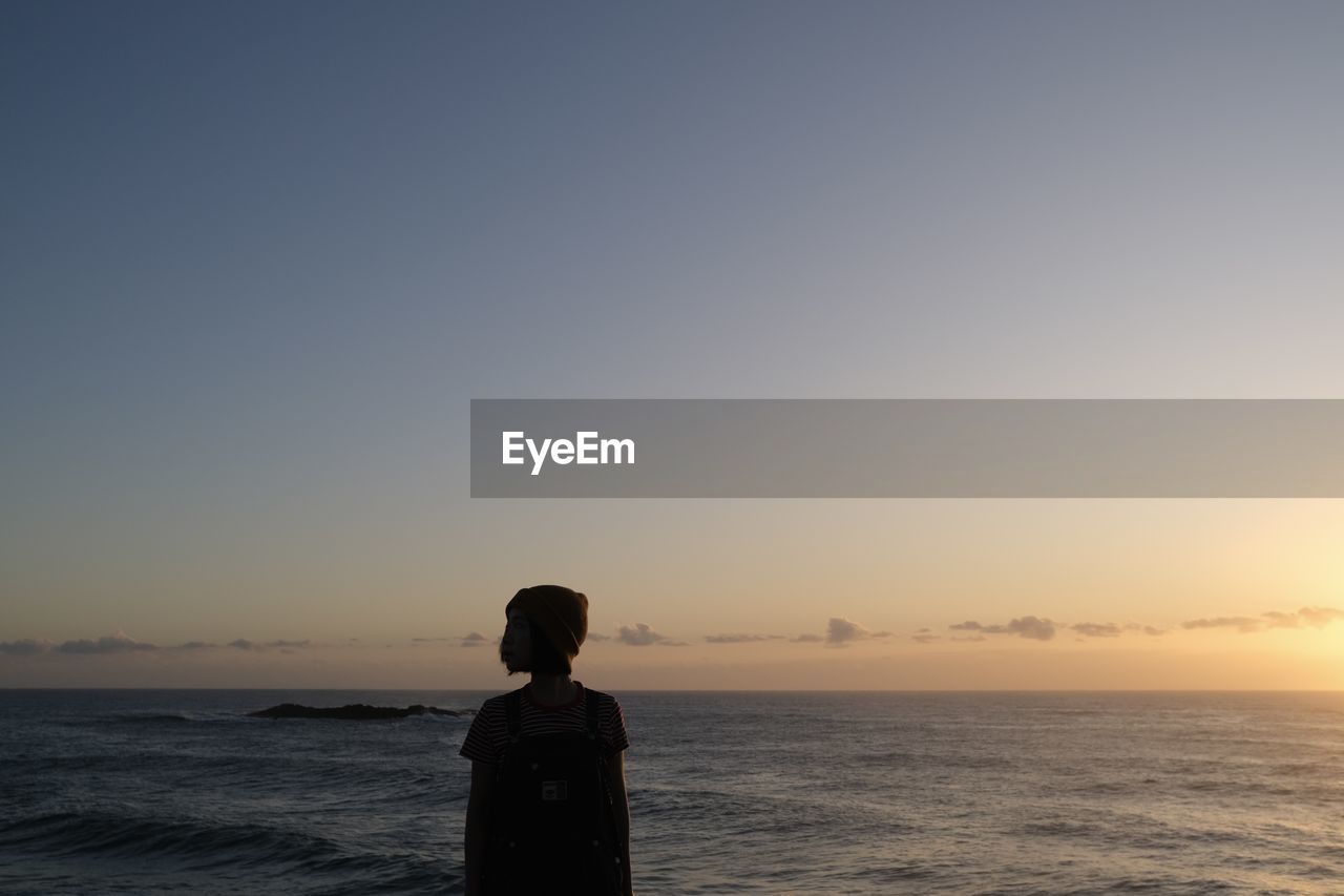 rear view of woman standing at sea against clear sky during sunset