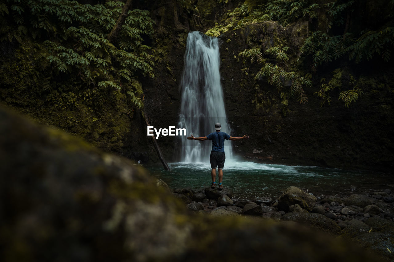 Man standing on rock against waterfall in jungle forest