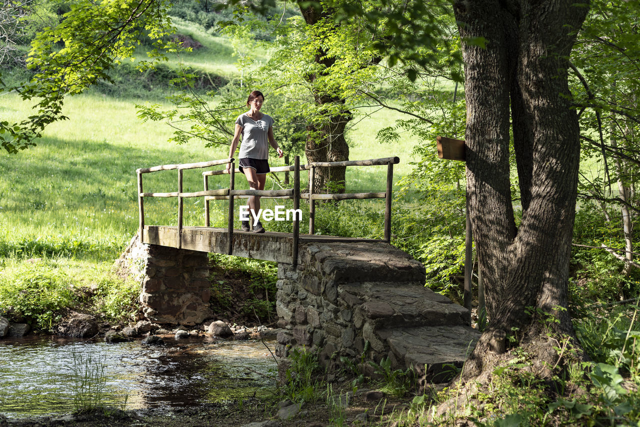 Active woman in a forest crossing a wooden bridge.