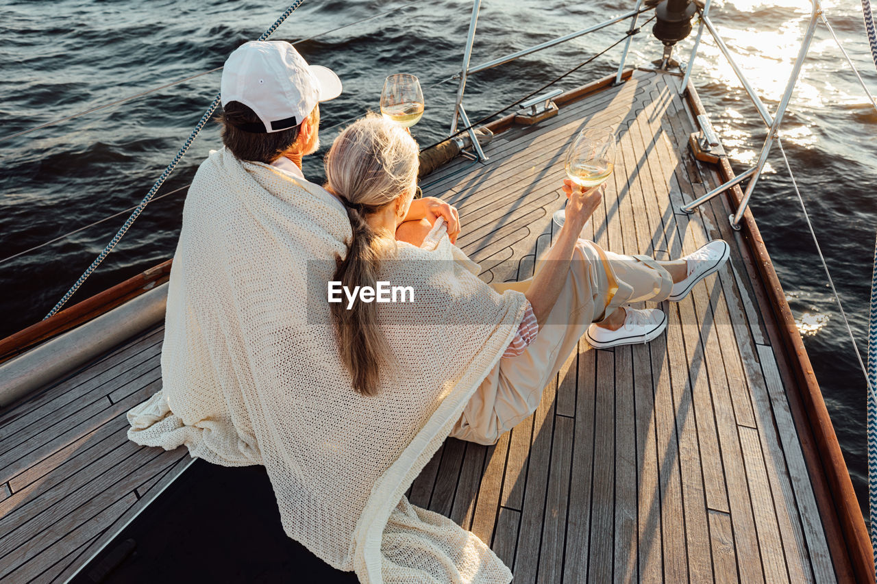 Rear view of couple sitting on boat sailing in sea