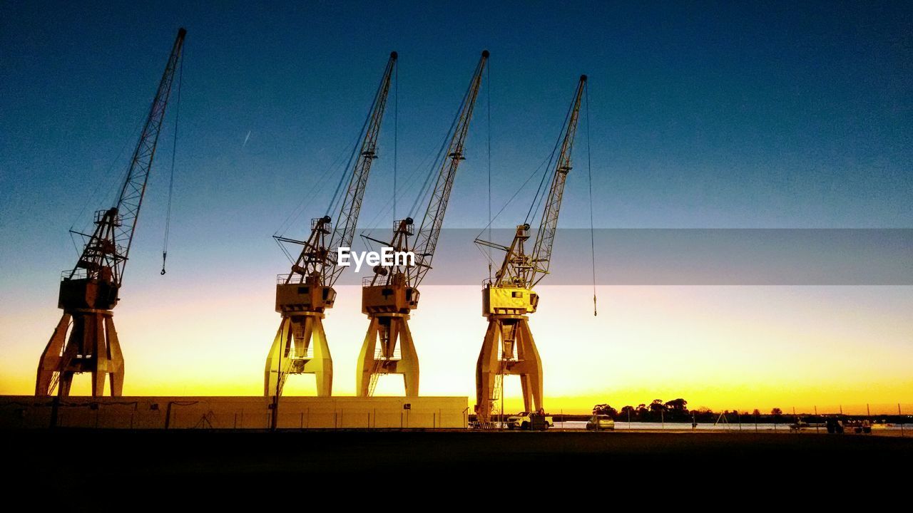 Cranes against sky during sunset