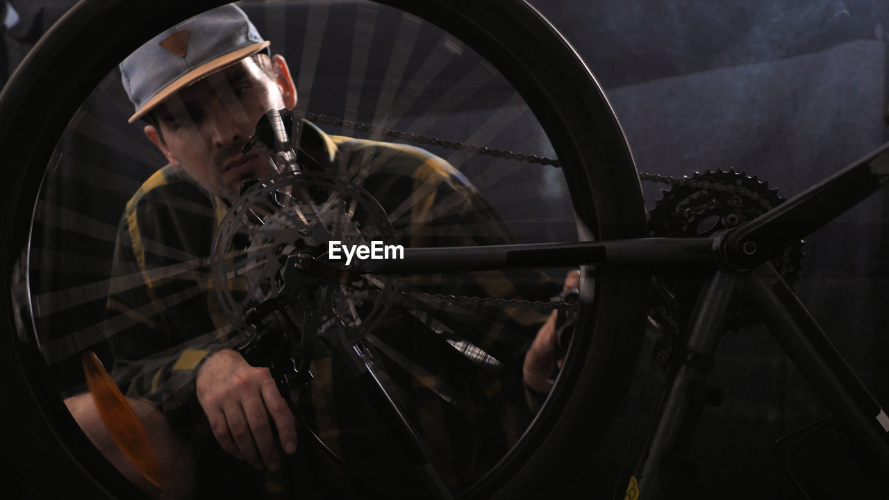 A man in a baseball cap and shirt is repairing a bicycle in a workshop. bicycle service, sports shop