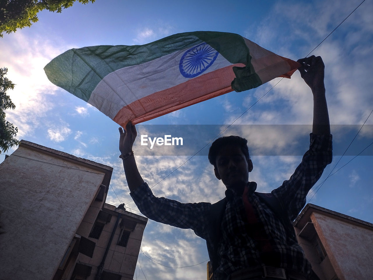 Low angle view of a boy waving indian flag against sky. 