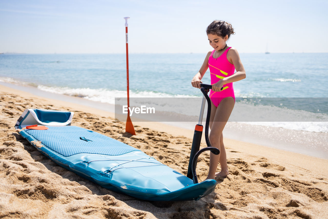 Little girl inflating a paddle surf on the beach