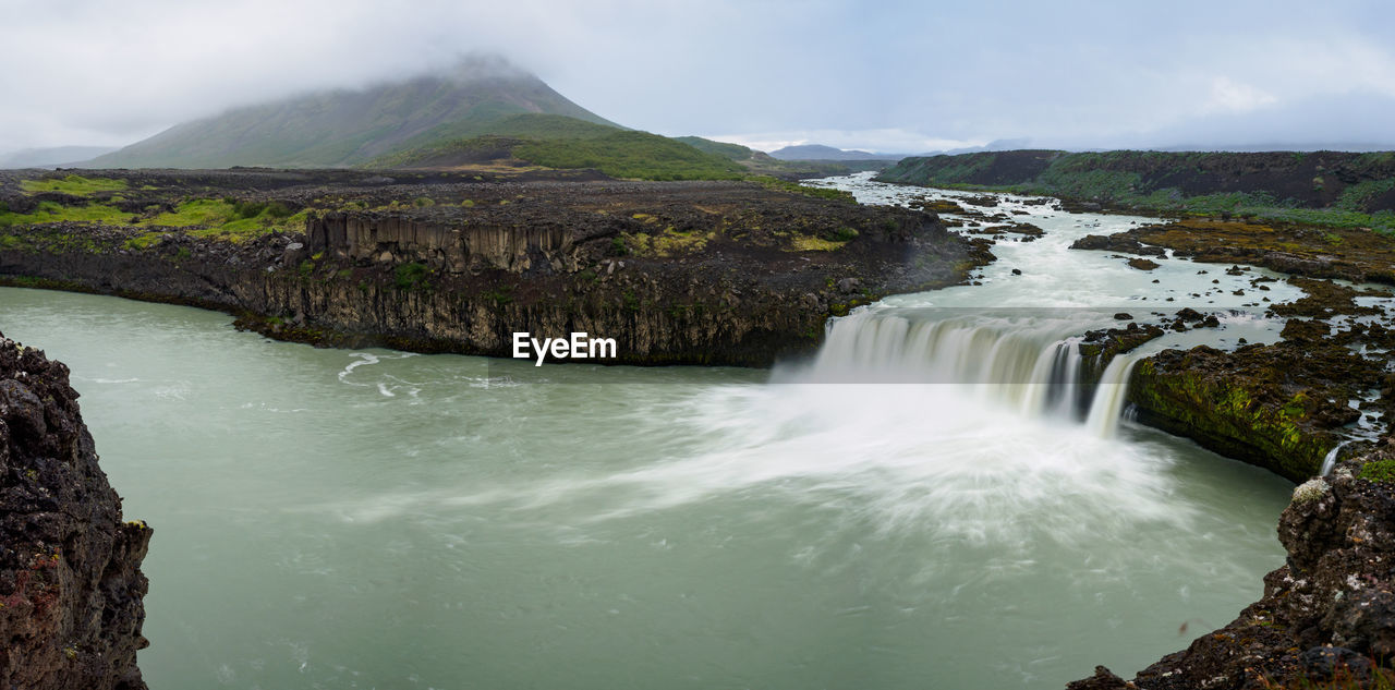 SCENIC VIEW OF WATERFALL AGAINST MOUNTAINS