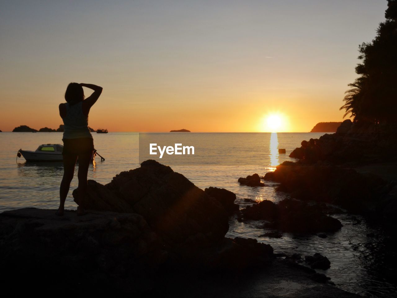 Silhouette woman standing on rock by sea against sky during sunset