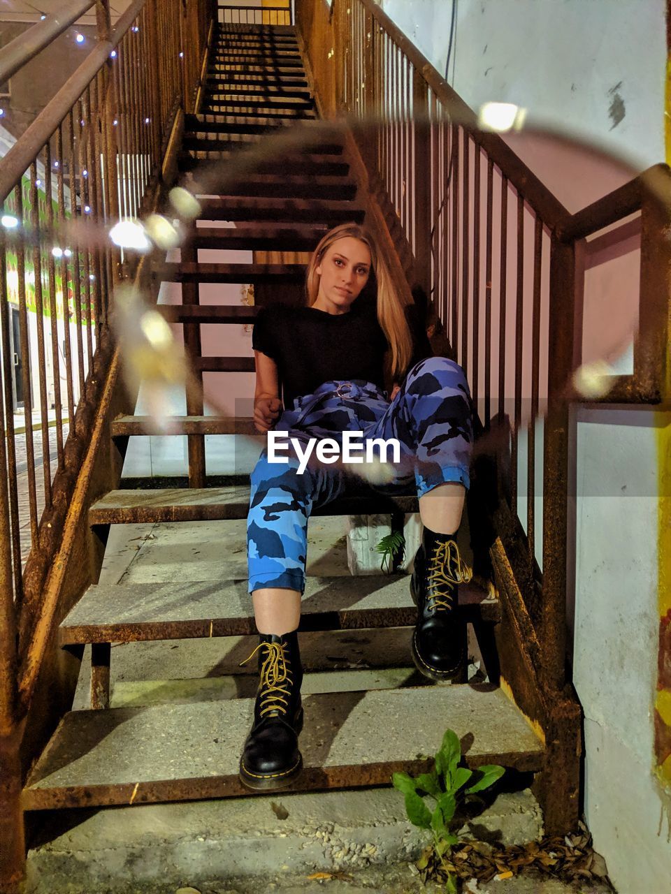 FULL LENGTH PORTRAIT OF WOMAN SITTING ON STAIRCASE OF BUILDING