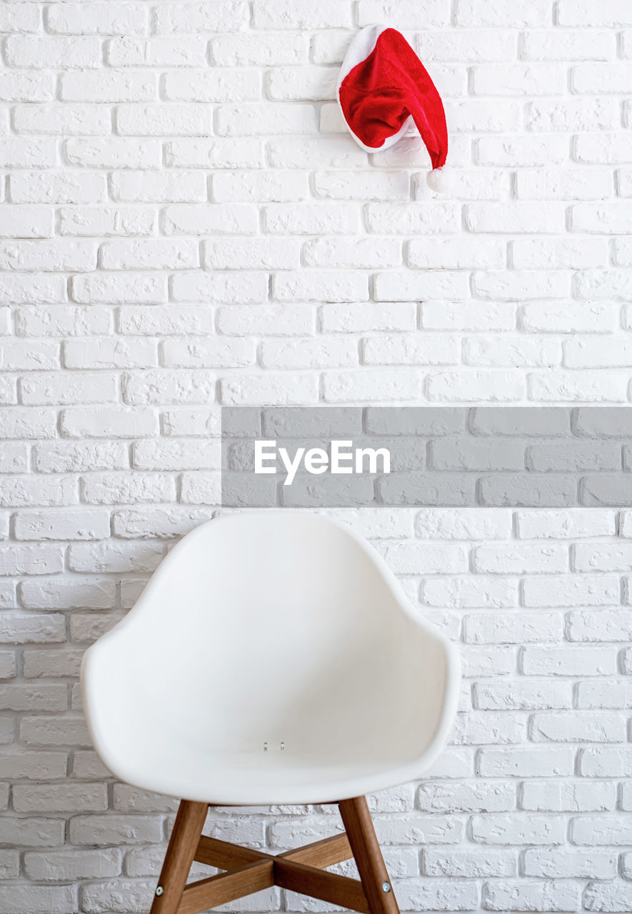 Minimal interior with a chair and a red santa hat hanging on the white brick wall with copy space