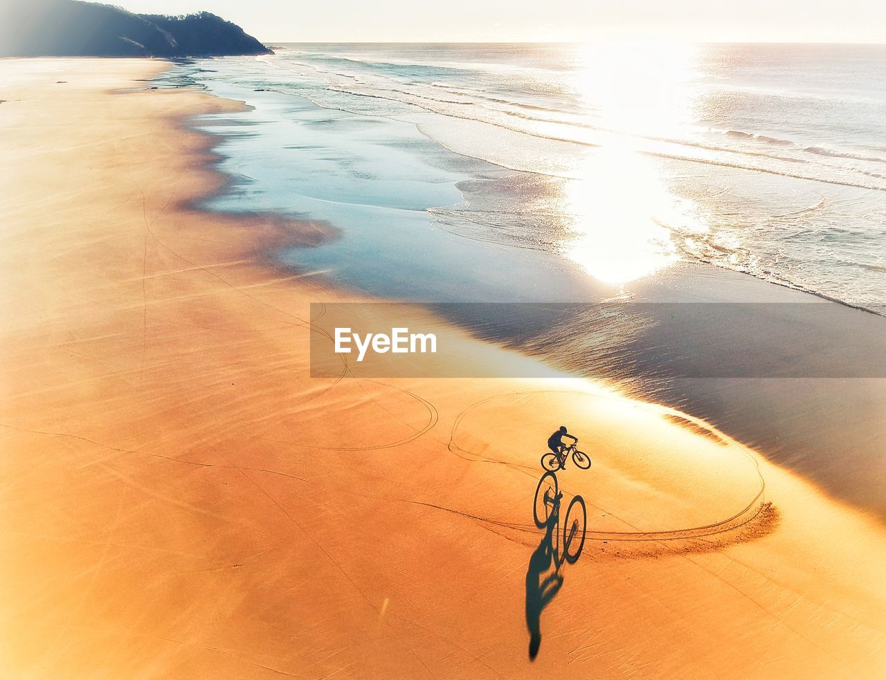 Boy riding bicycle on beach during sunset