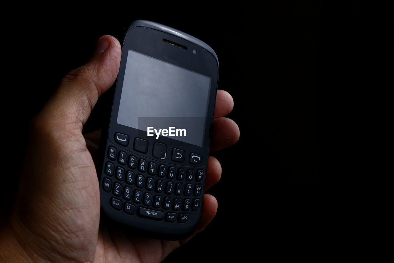 Cropped hand of person holding smart phone against black background