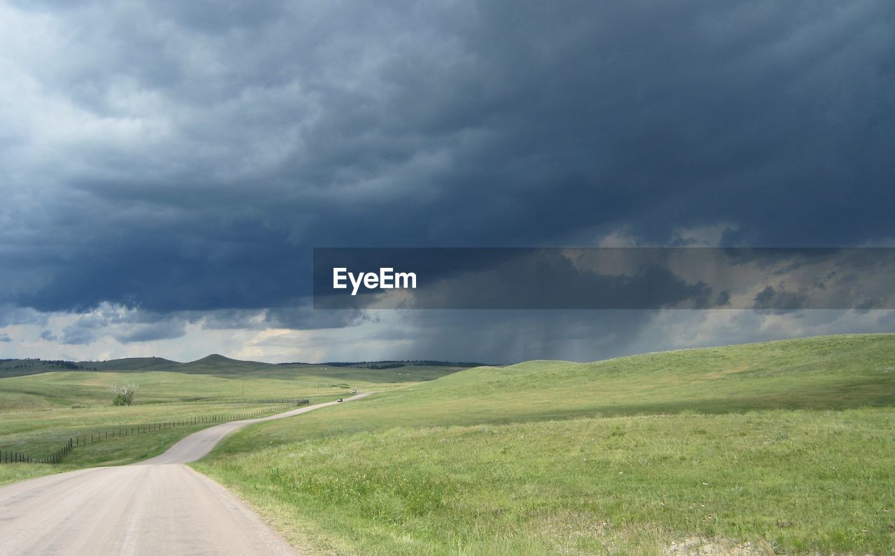 Road passing through field against cloudy sky