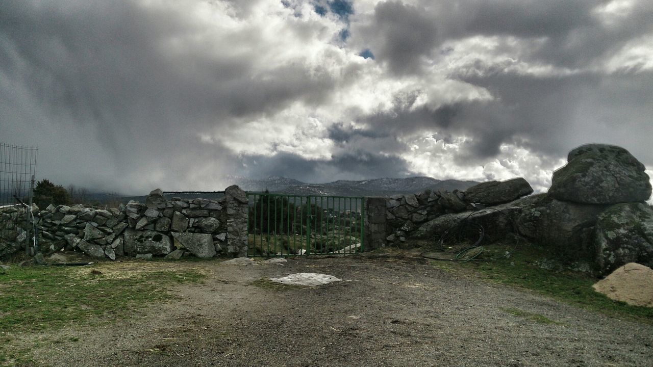 Closed gate on field against cloudy sky