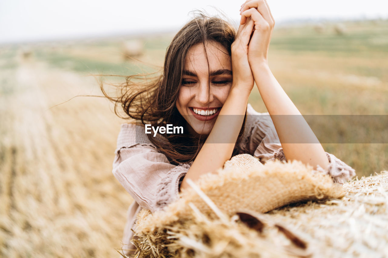 Close-up of smiling young woman with eyes closed by hay bale