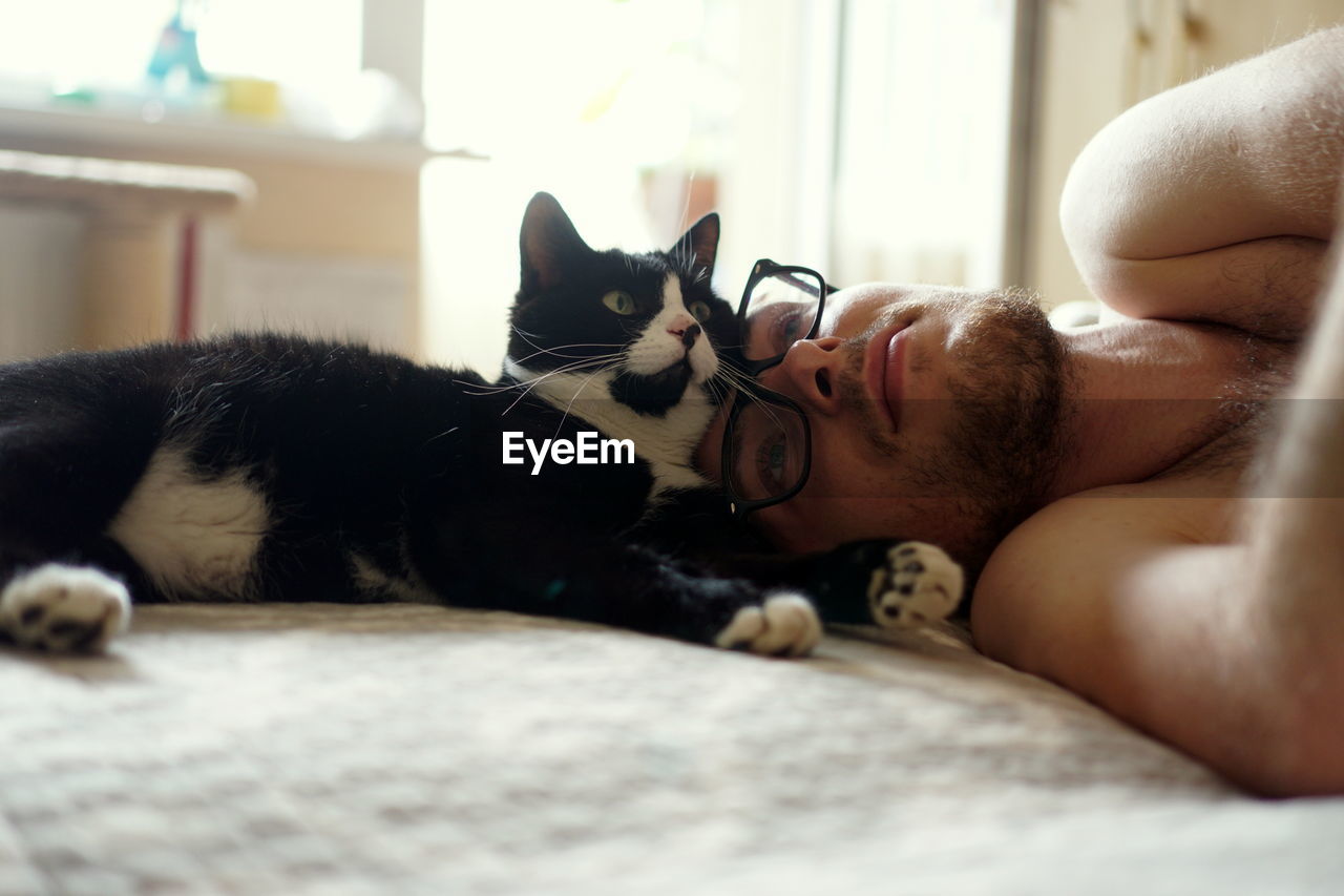 Man lying with cat on bed at home