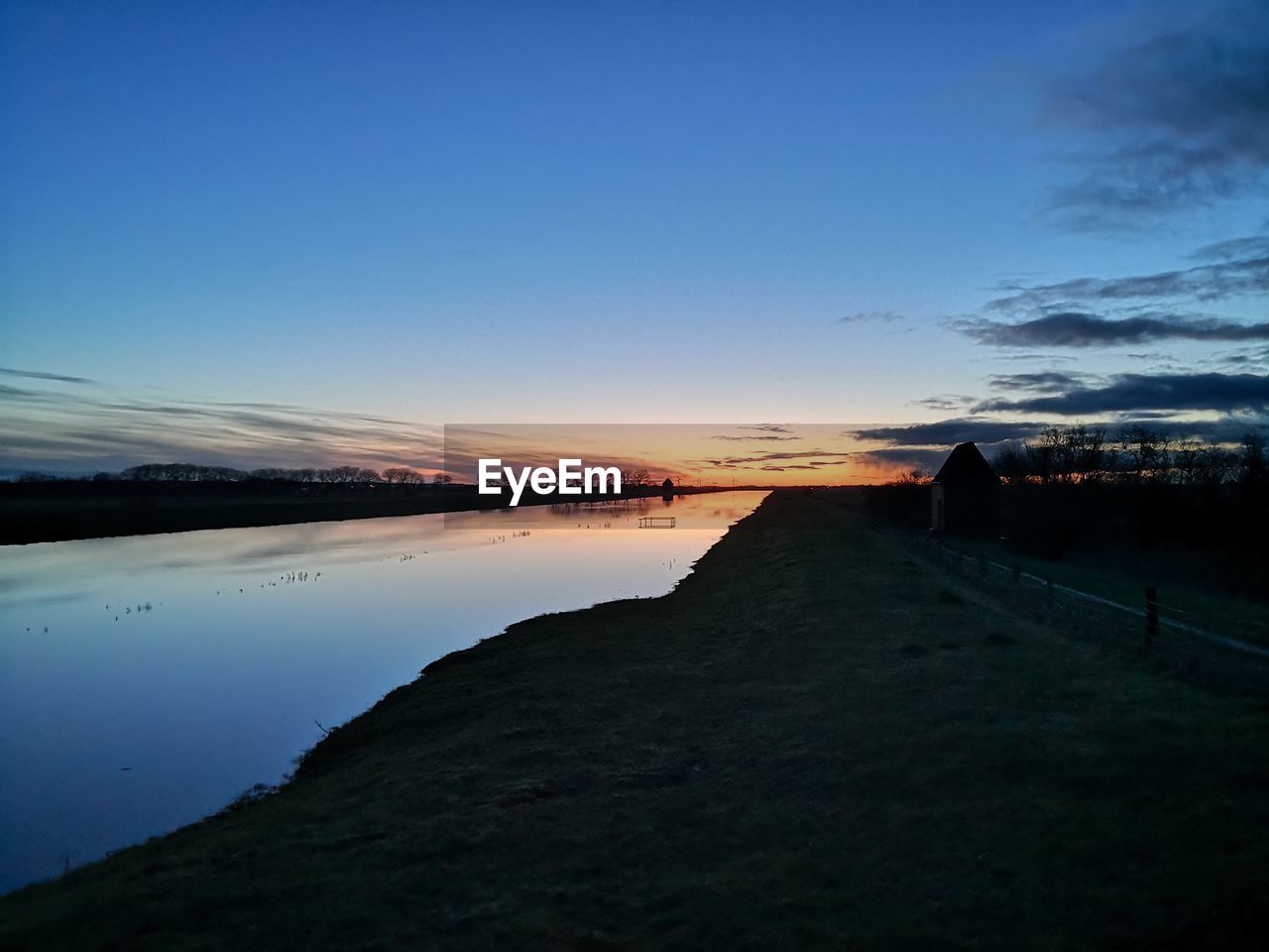 SCENIC VIEW OF LAKE AGAINST BLUE SKY DURING SUNSET