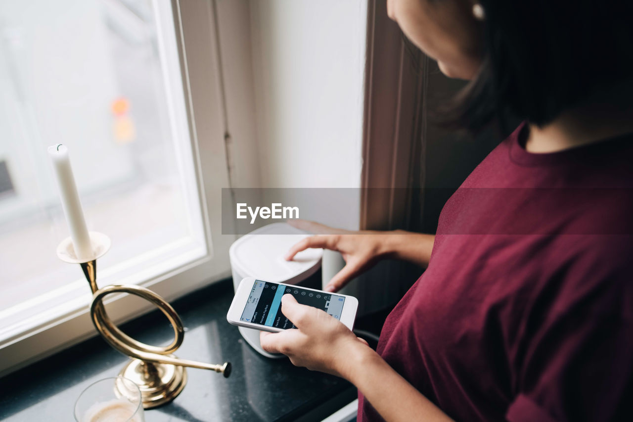 Midsection of woman using smart phone while standing by window