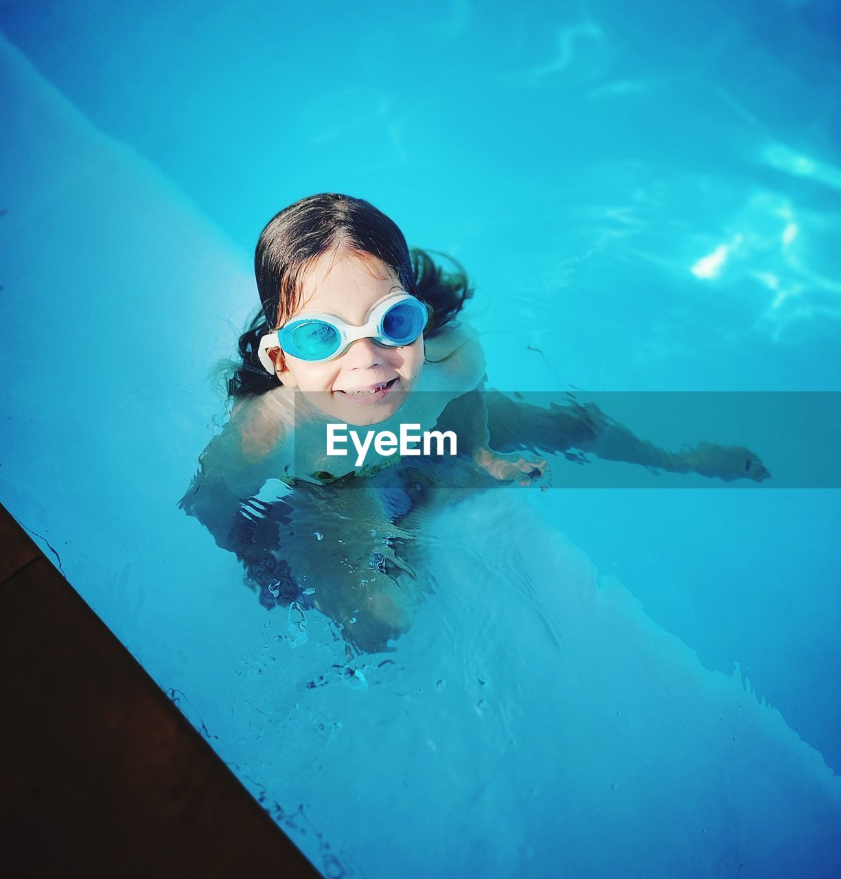 My little girl is enjoying sun-lit swimming pool in blue, pool color matching goggles. 