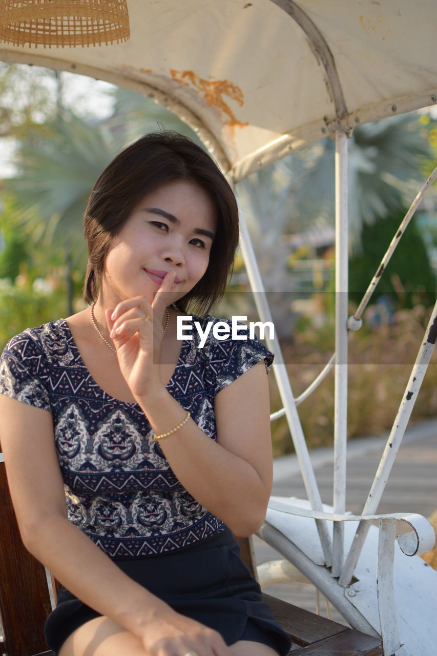 Portrait of smiling young woman with finger on lips sitting on bench