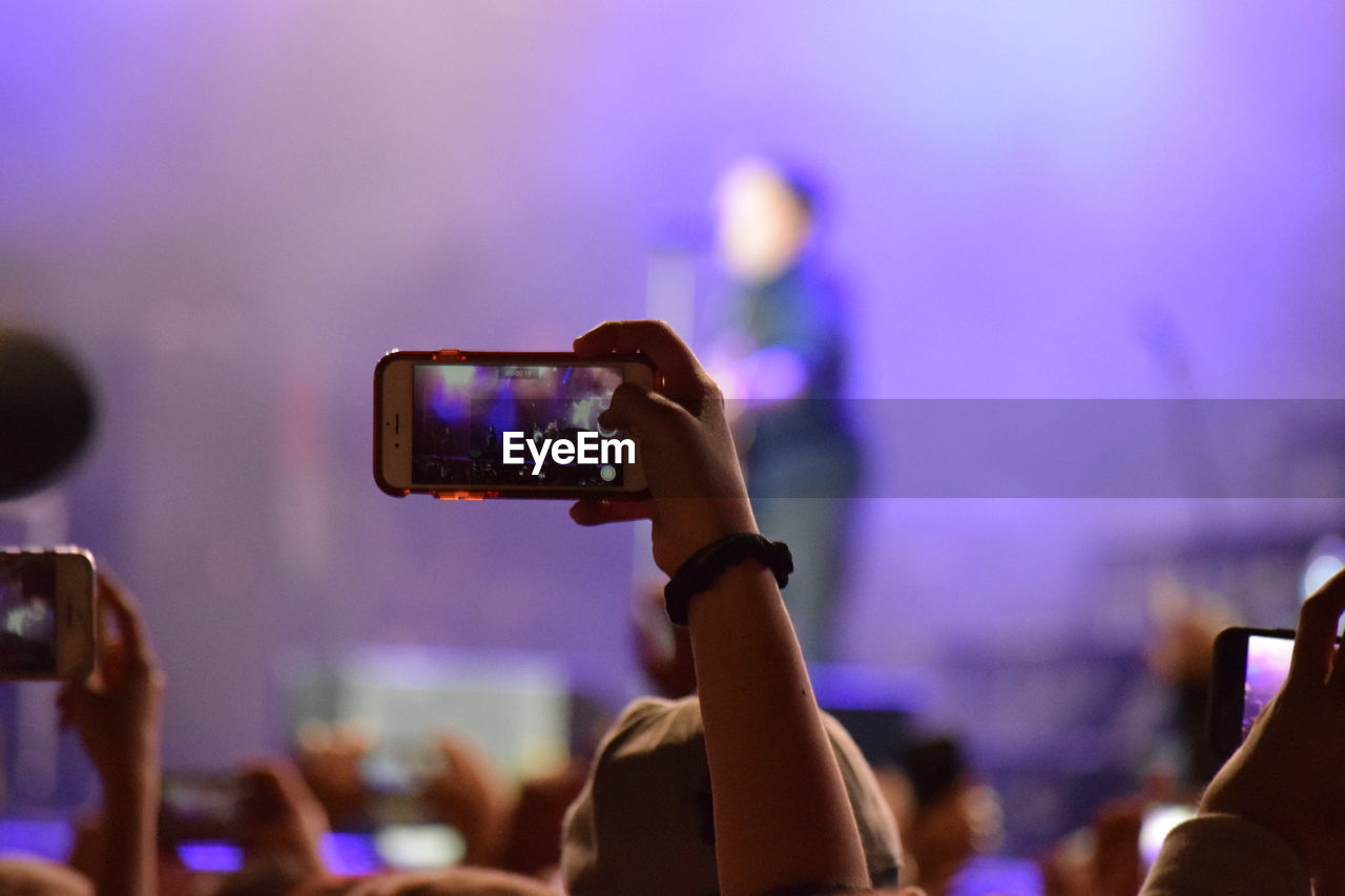 Cropped image of woman photographing musician on stage