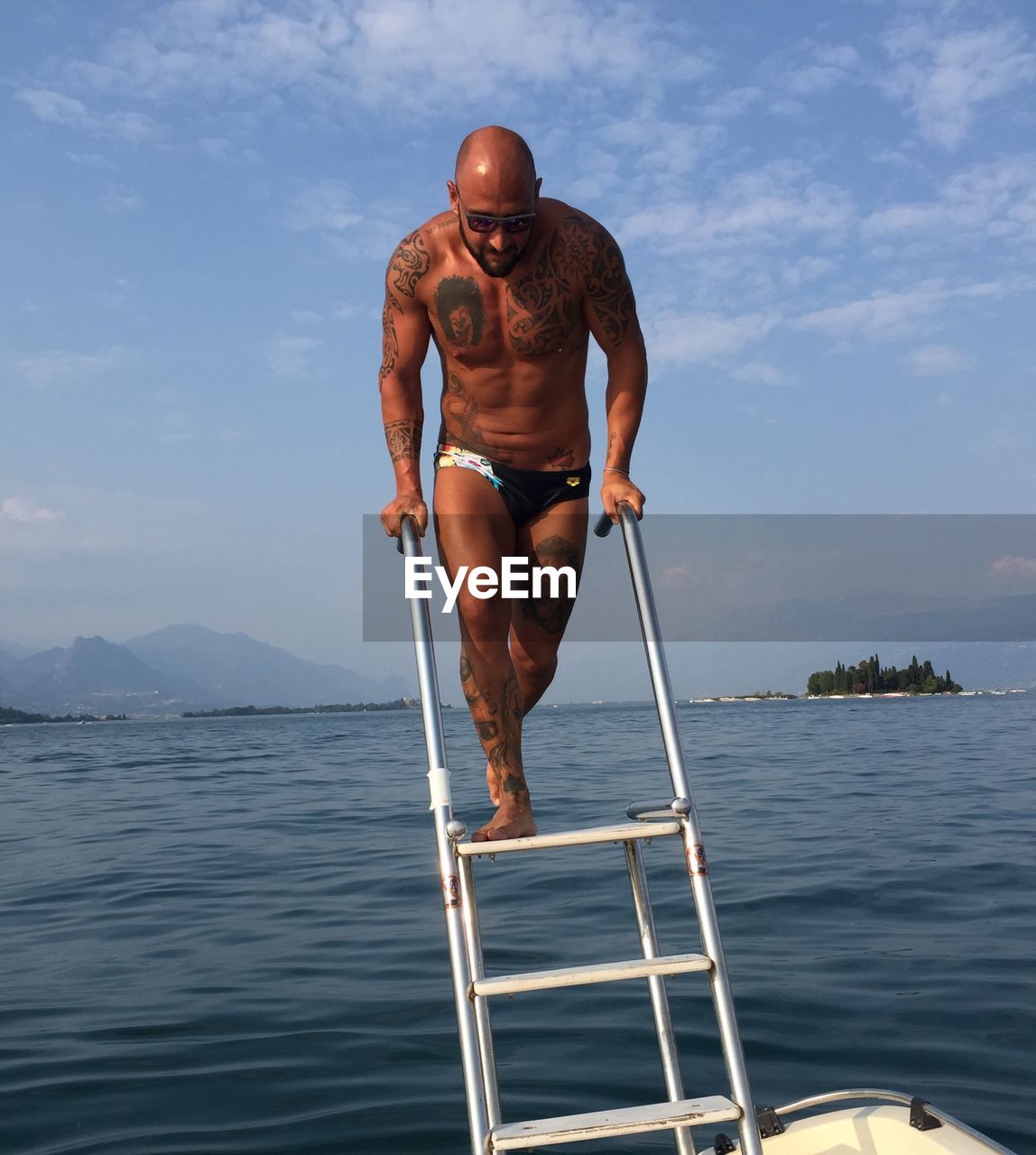 Full length of shirtless man standing by sea on ladder