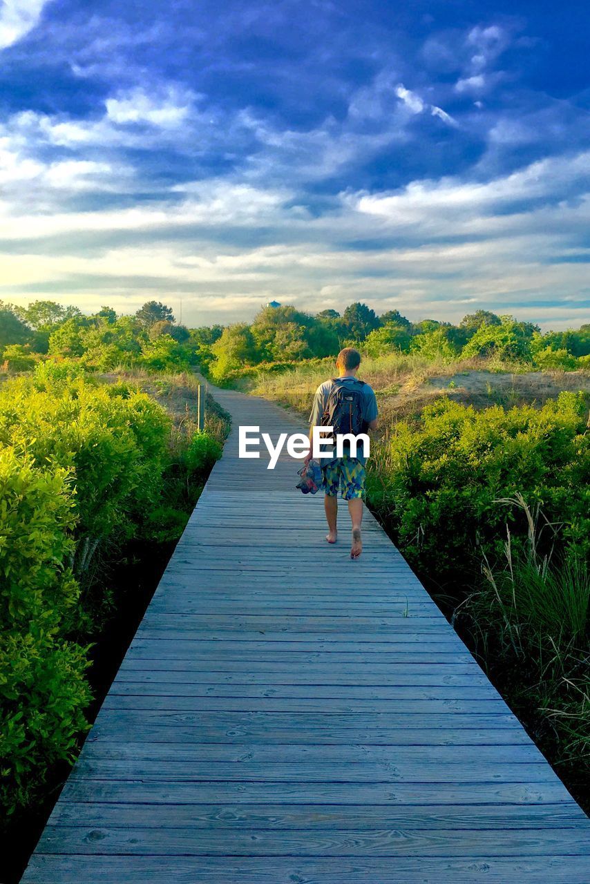 REAR VIEW OF MAN WALKING ON WALKWAY