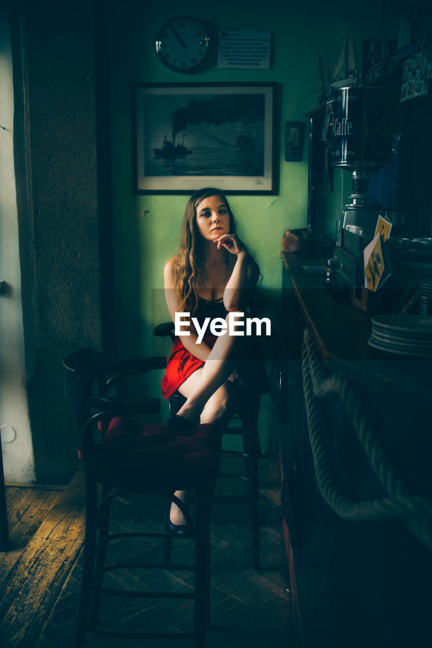 FULL LENGTH PORTRAIT OF WOMAN SITTING ON CHAIR AT HOME