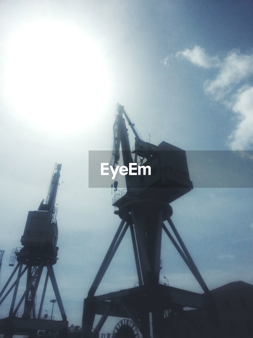 Low angle view of cranes at harbor against cloudy sky