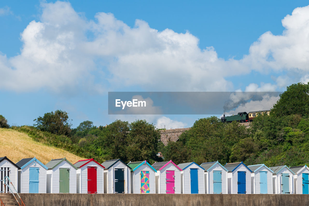 Colourful beach houses. row of  beach huts with steam train on stone viaduct against blue sky.