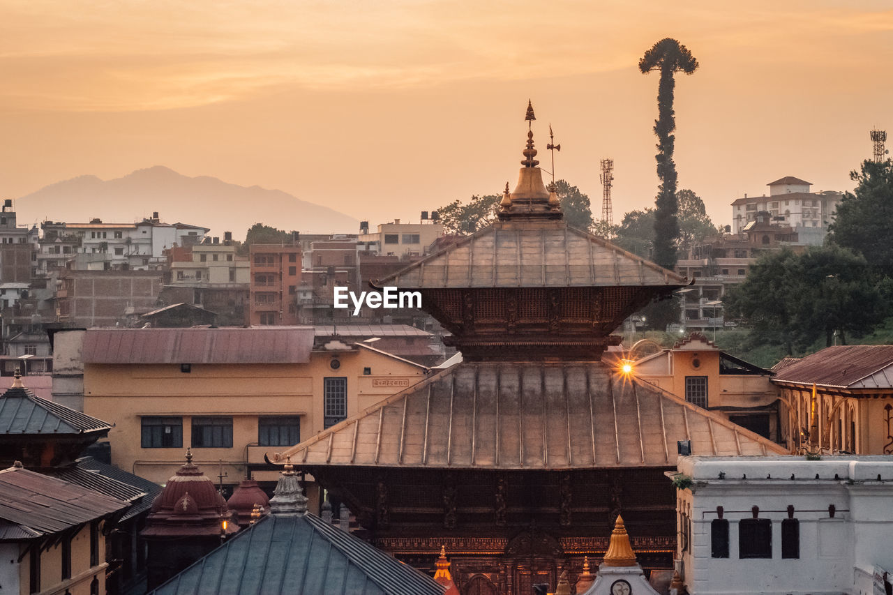 Temple and buildings in city against sky during sunset