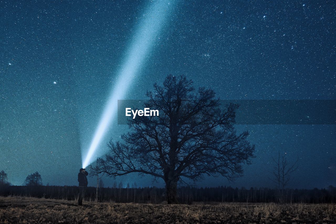 Man with flashlight standing against star field on field