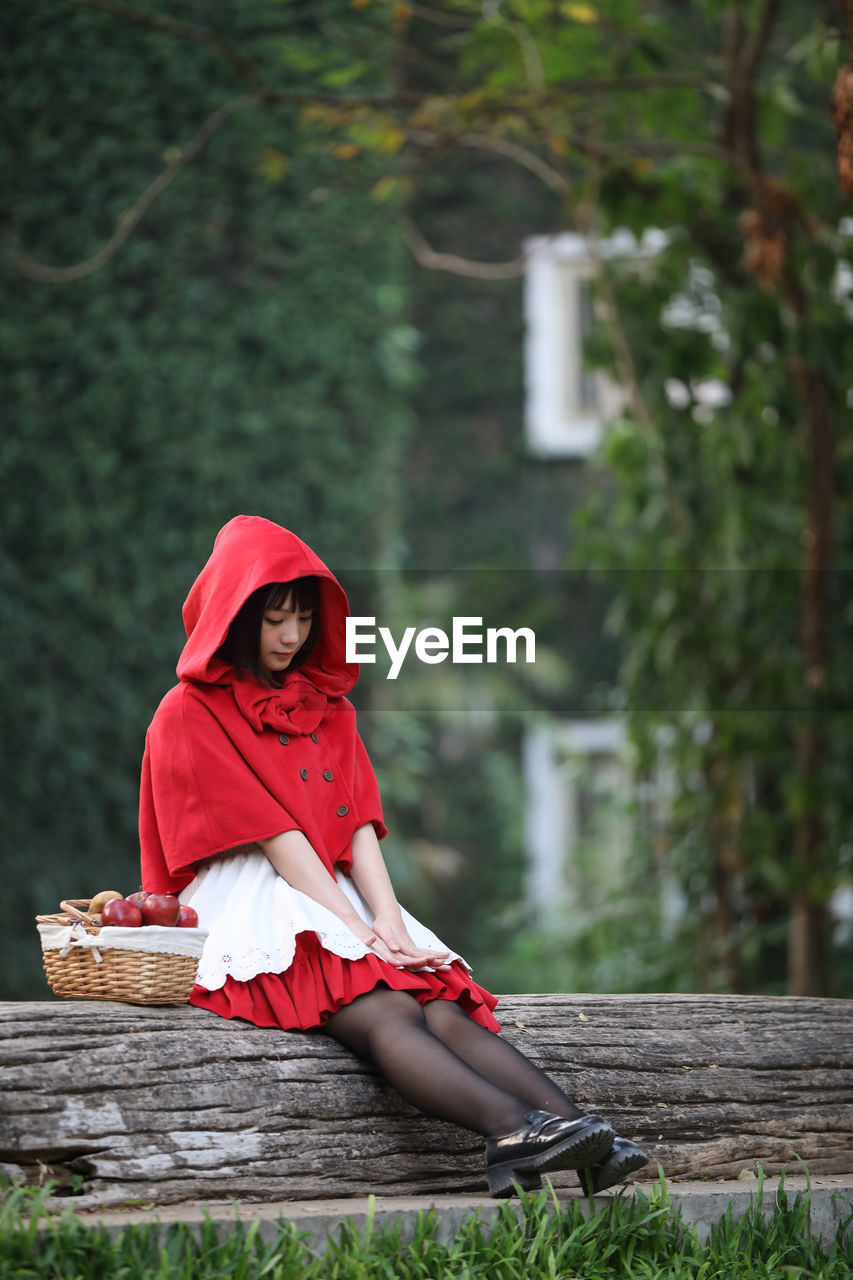 Young woman with fruits in basket looking away while sitting against tree