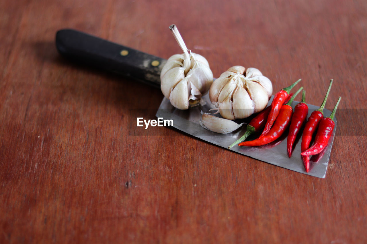 Close-up of red chili peppers and garlic on a knife against wooden table