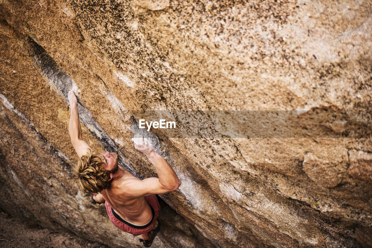 High angle view of shirtless hiker climbing rock