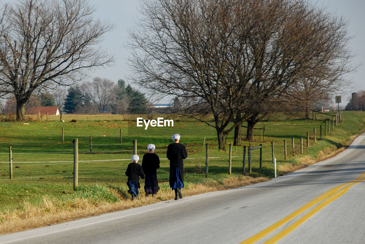 Rear view of amish women walking on road amidst bare trees