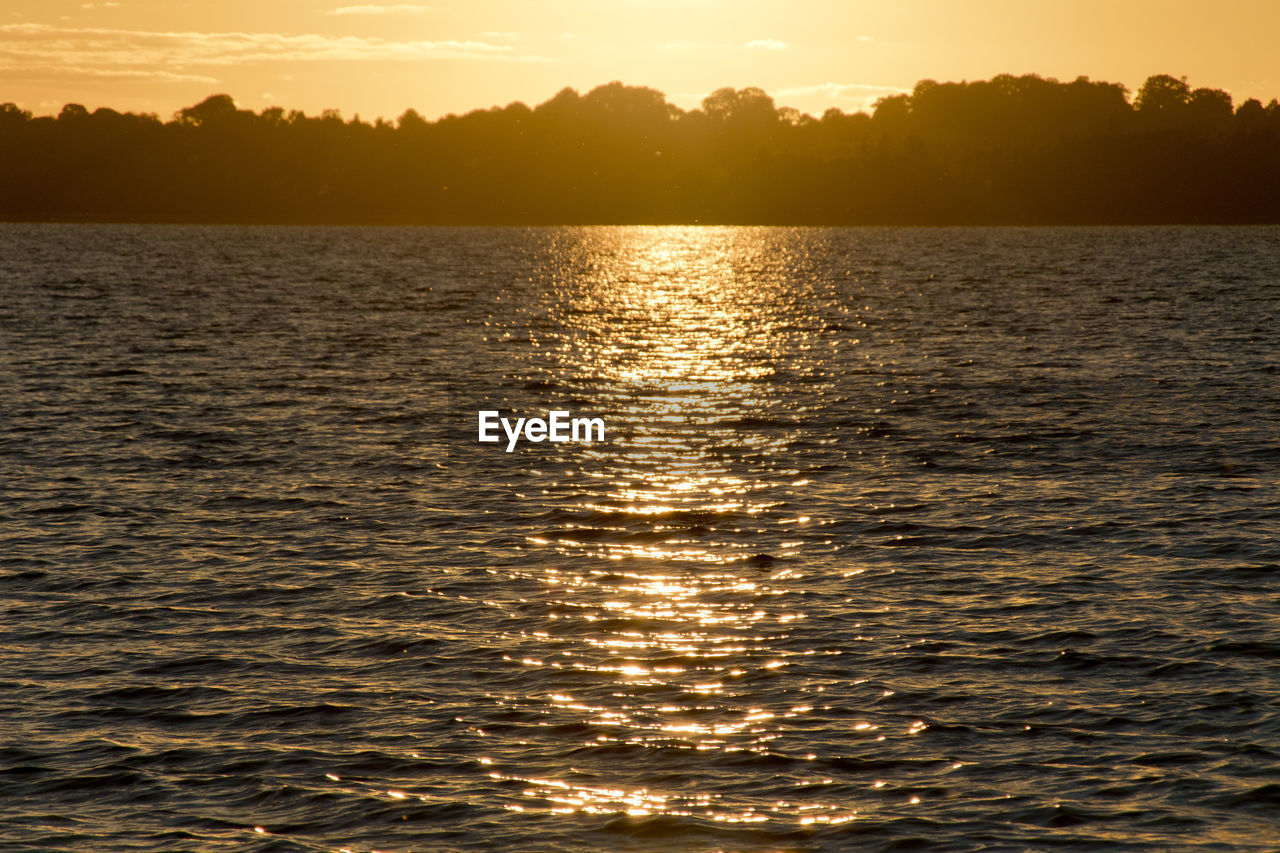 Sunset reflected on lake surface with silhouette of far shore