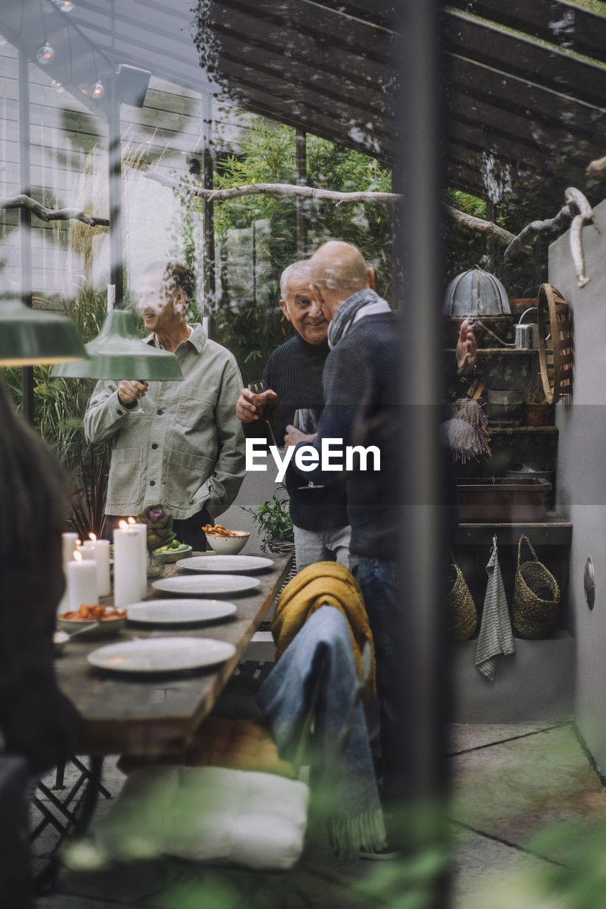 Male friends talking to each other at dinner party seen through glass