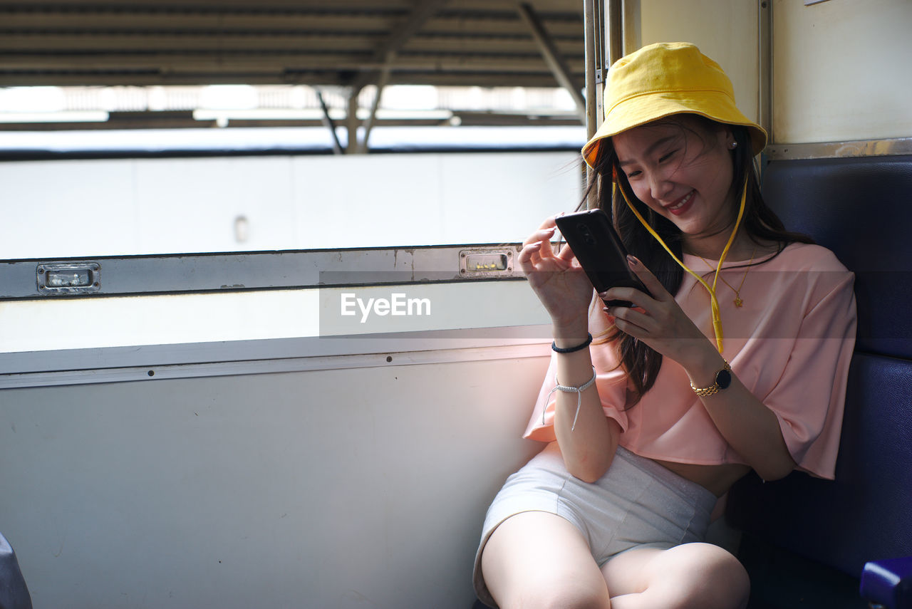 Smiling young woman using mobile phone while sitting in train