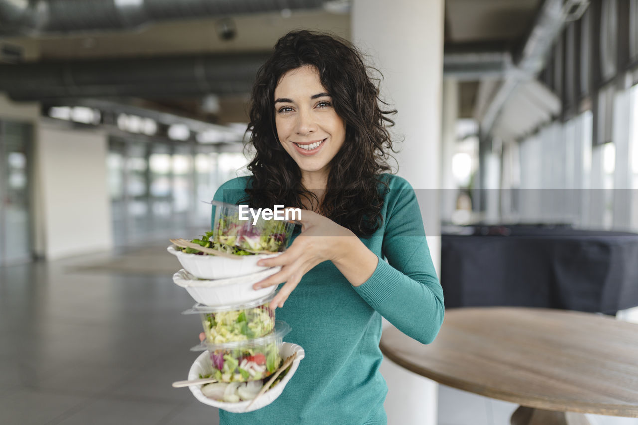 Happy businesswoman holding stack of salad in office