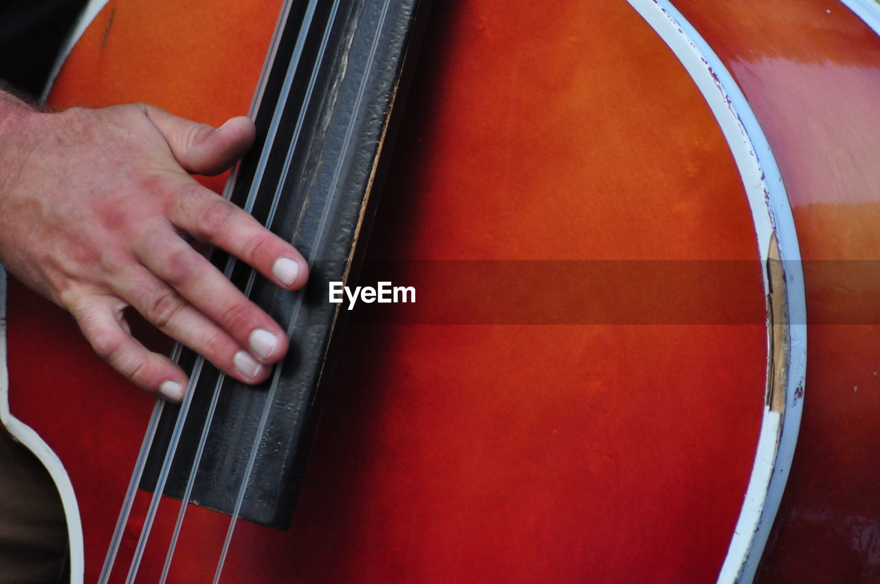 hand, musical instrument, music, cello, musician, arts culture and entertainment, one person, musical equipment, string instrument, double bass, bowed string instrument, performance, red, adult, skill, close-up, musical instrument string, violone, guitar, acoustic guitar, midsection, string, violin, performing arts event, classical music, holding, men