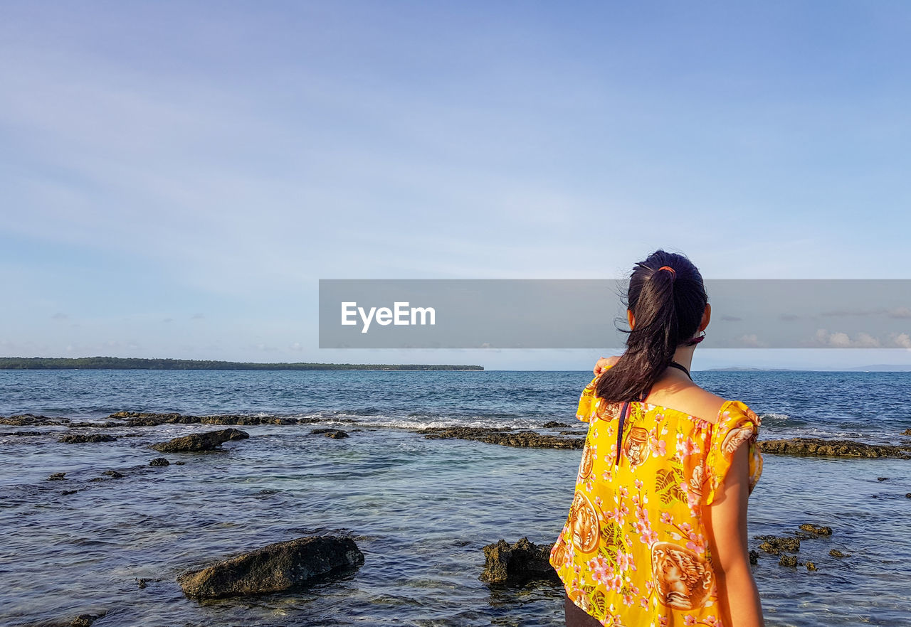 Rear view of woman standing at beach against sky