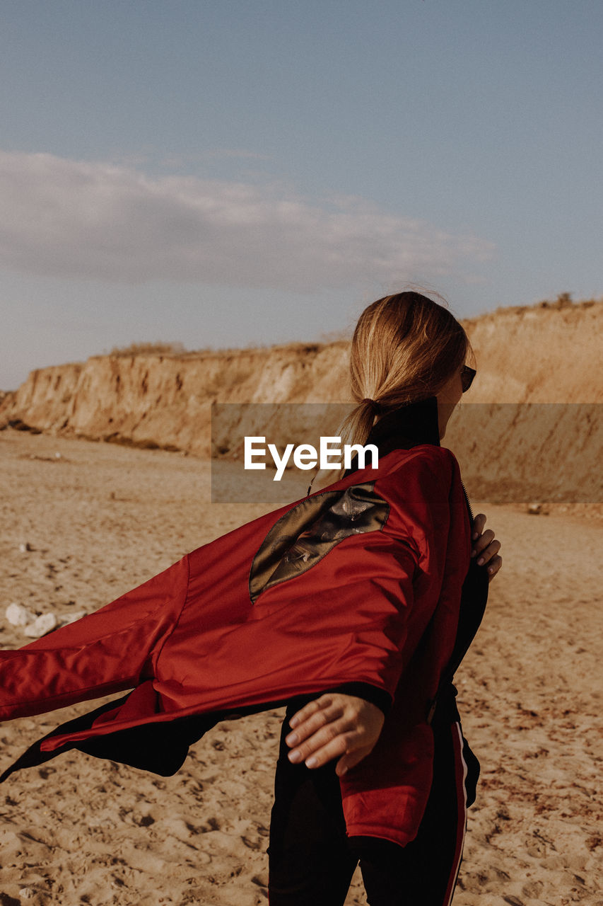 Side view of woman holding jacket against mountain and sky