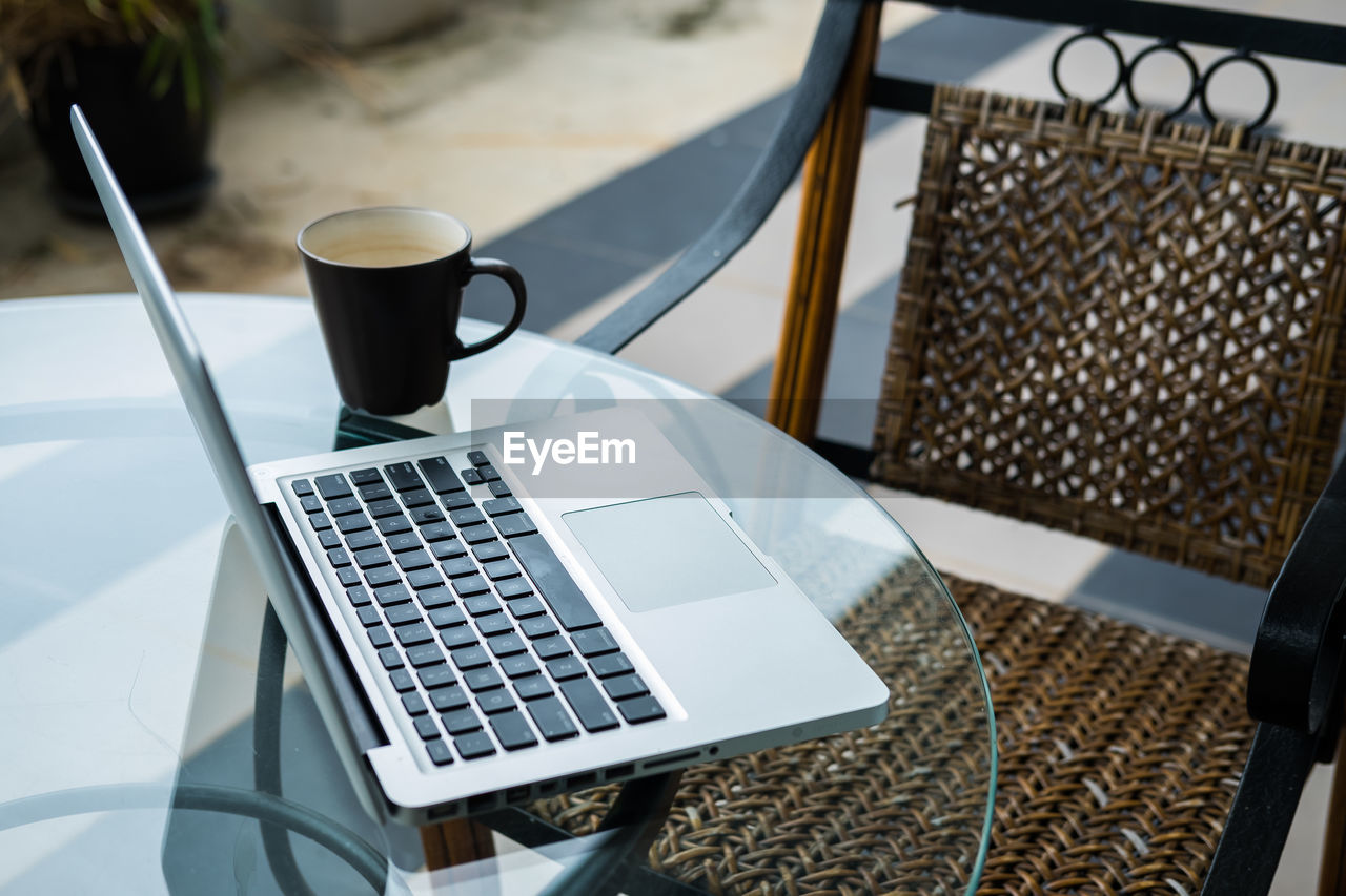 A cup of coffee, a laptop, a table and chair alongside each other