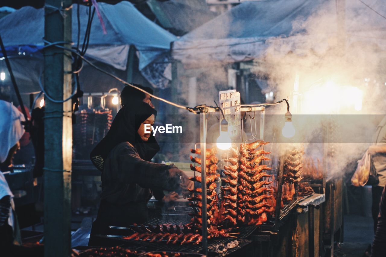 Woman preparing food in market stall at night