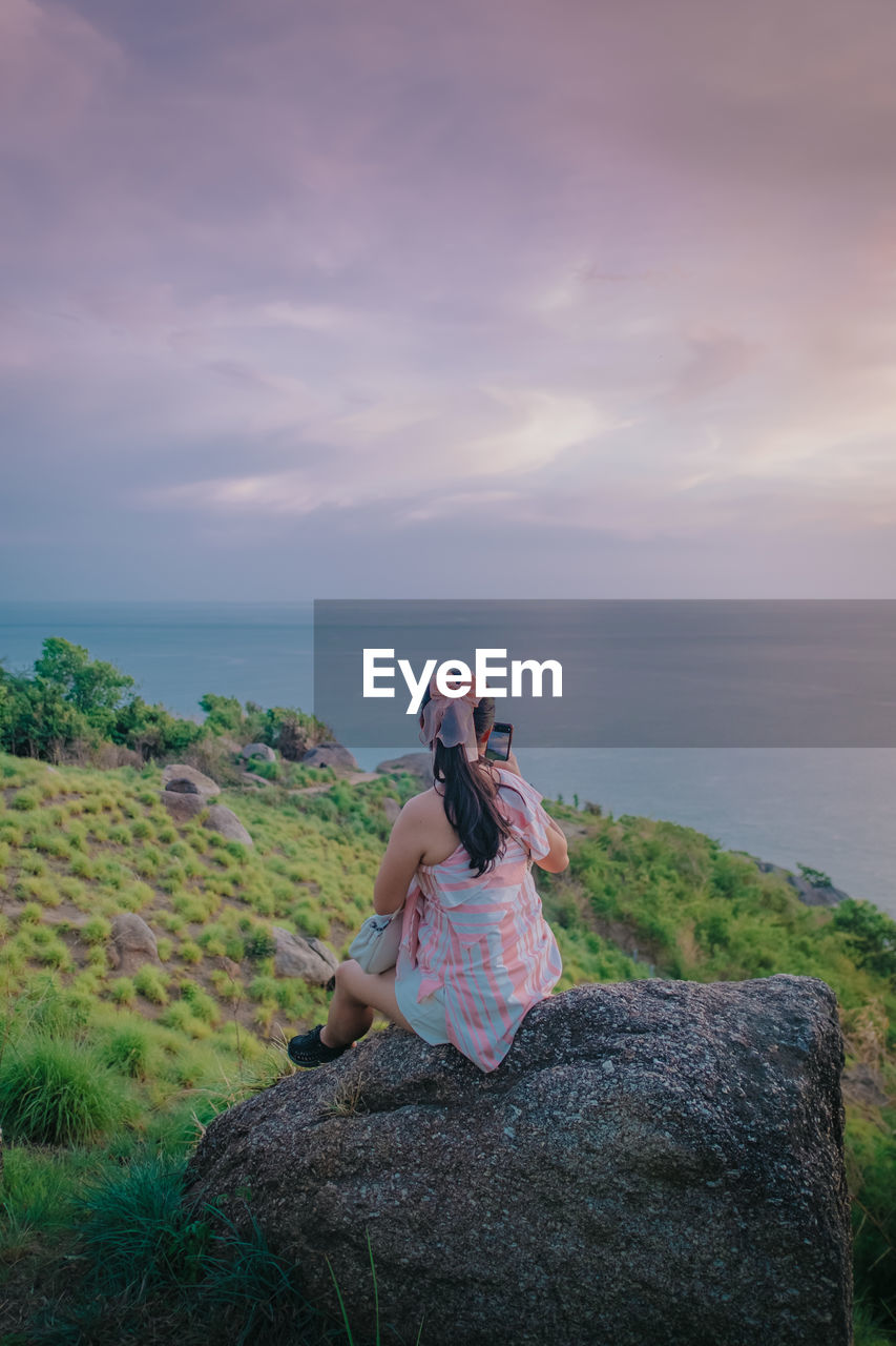 Rear view of woman sitting on rock against sky