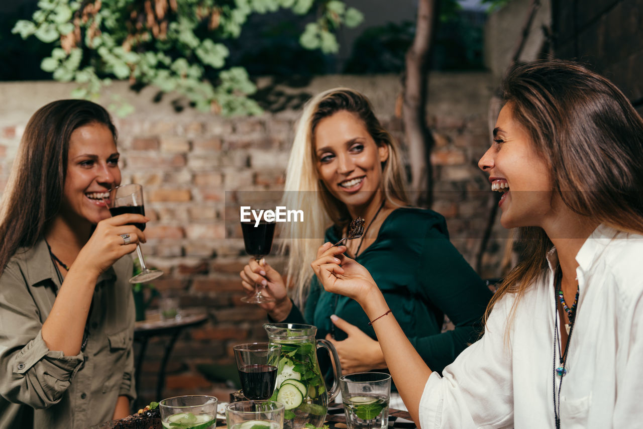 Female friends having food and drinks at outdoors restaurant during night