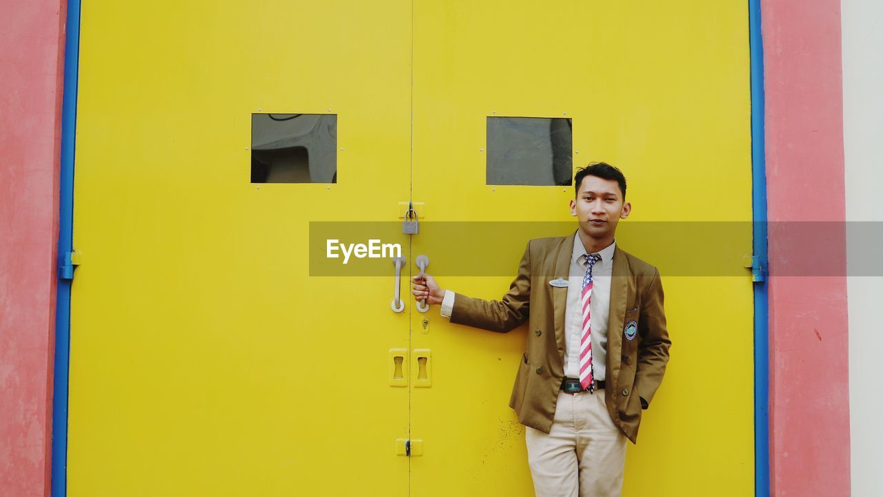 Portrait of smiling young man standing against yellow door