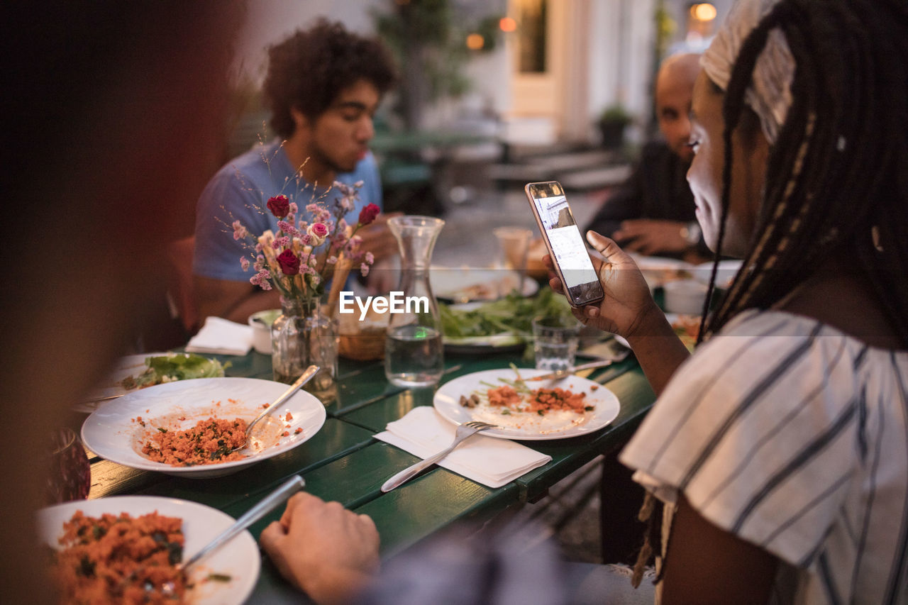 Young woman using mobile phone while having dinner with friends during garden party