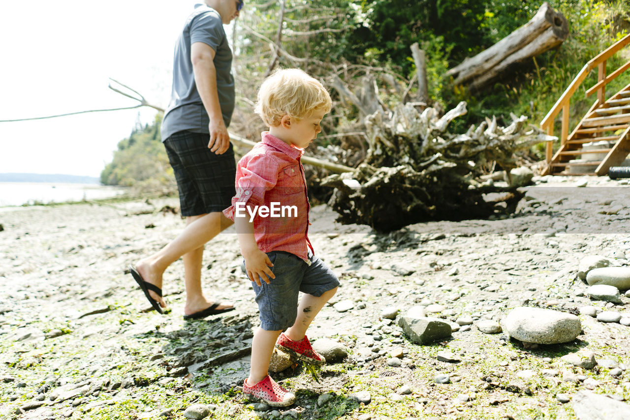 Side view of a father and son walking on a rocky beach on a sunny day