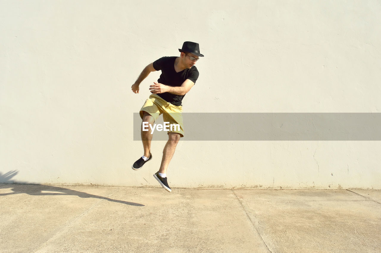 Full length of young man jumping on footpath against wall